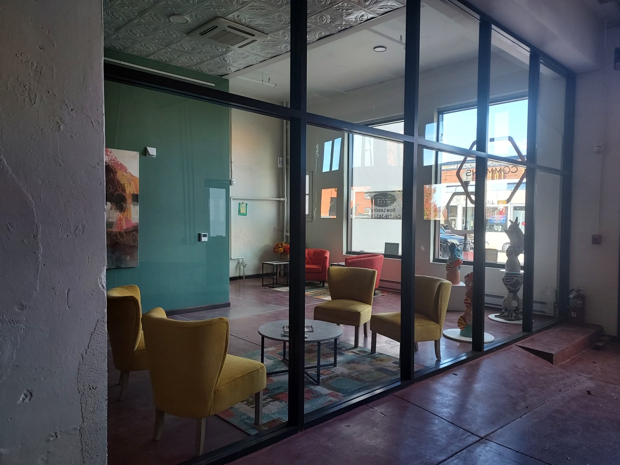 A view of a meeting space in The Commons at Space to Create. There is contemporary furniture beside large windows that look out onto Main Street.