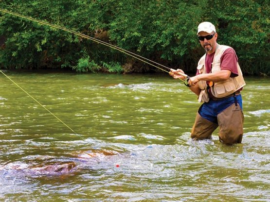 man fly fishing with waders standing in river